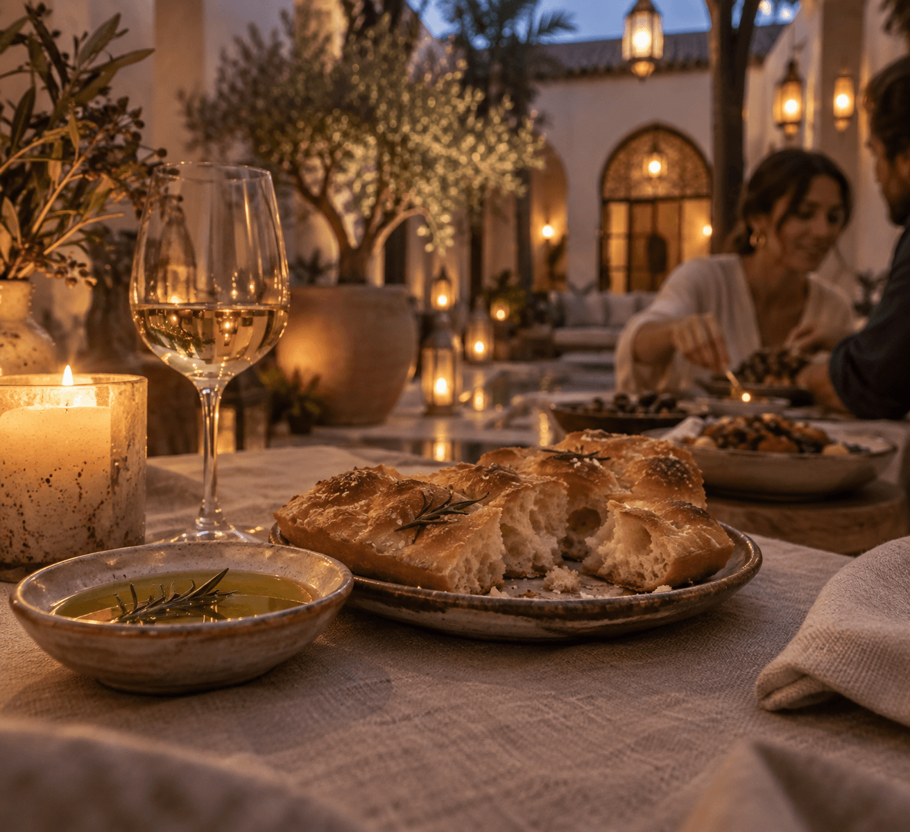 Torn focaccia and olive oil on linen by candlelight, lanterns glowing in the riad courtyard behind
