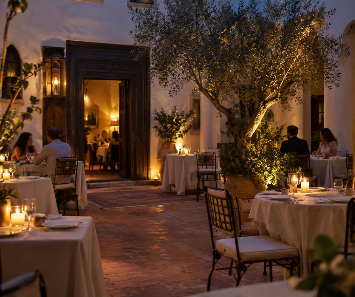 Guests dining beneath an olive tree in the courtyard at blue hour