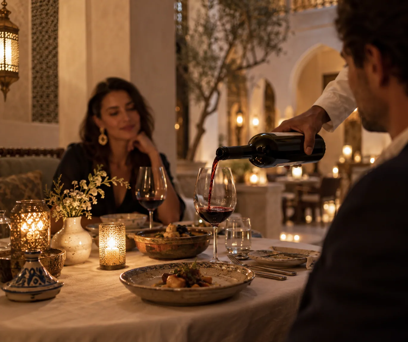 A host pouring red wine beside a candlelit dinner
